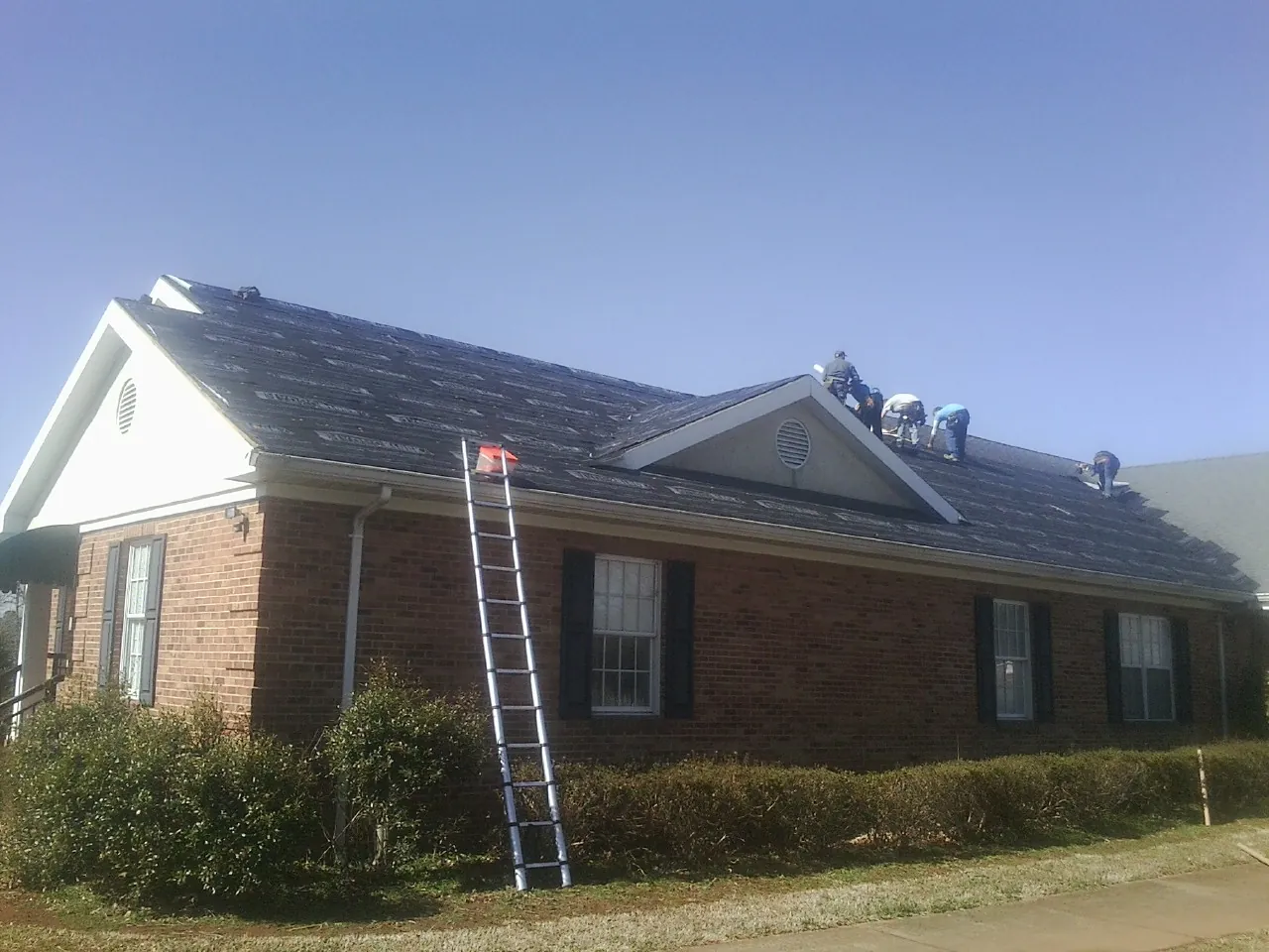 Crew tearing shingles off a brick ranch roof with a ladder set — Metal Roof Repair work by our crew in Nicholasville