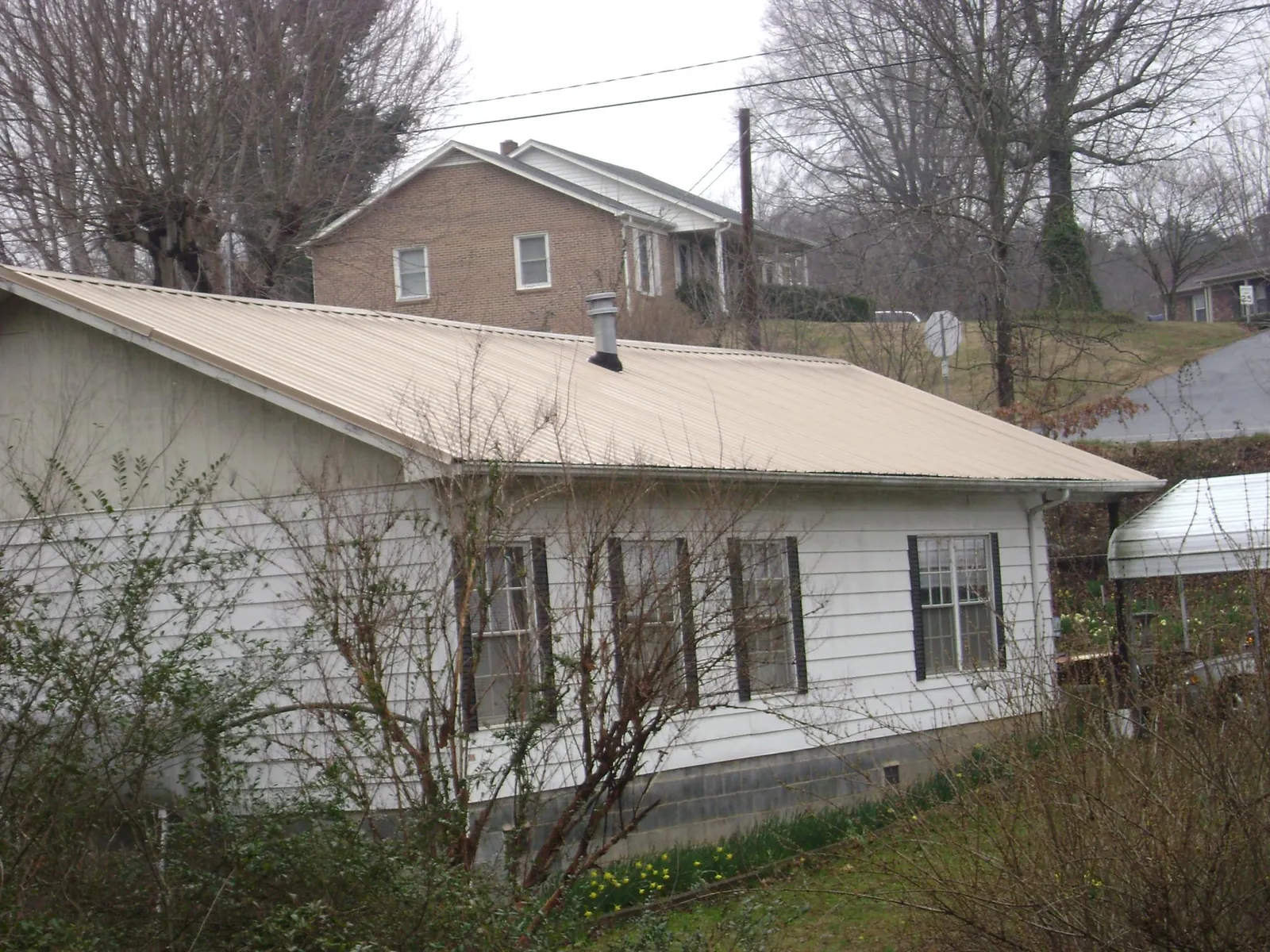 Tan metal roof on a white sided house set into a hillside — Commercial Roofing by Roofing Brothers in Nicholasville